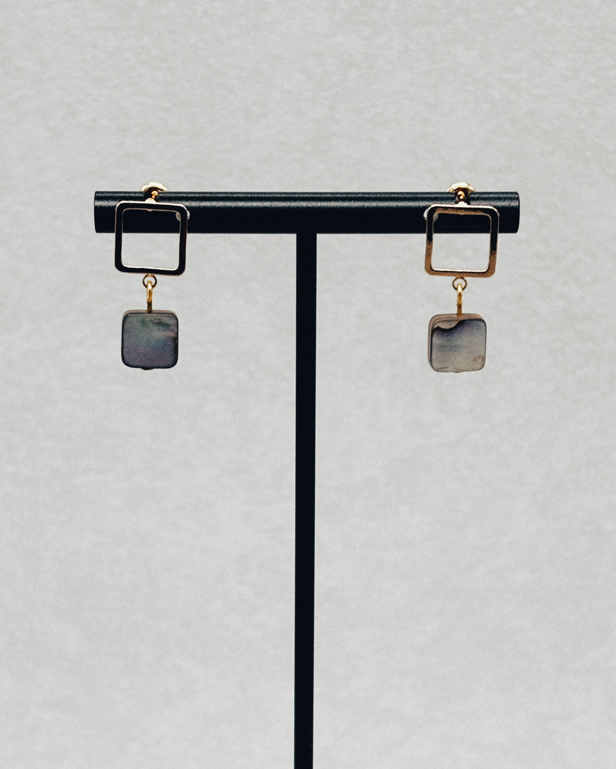 Abalone Gold Square Studs with square gold frames and iridescent abalone stone drops displayed on a stand