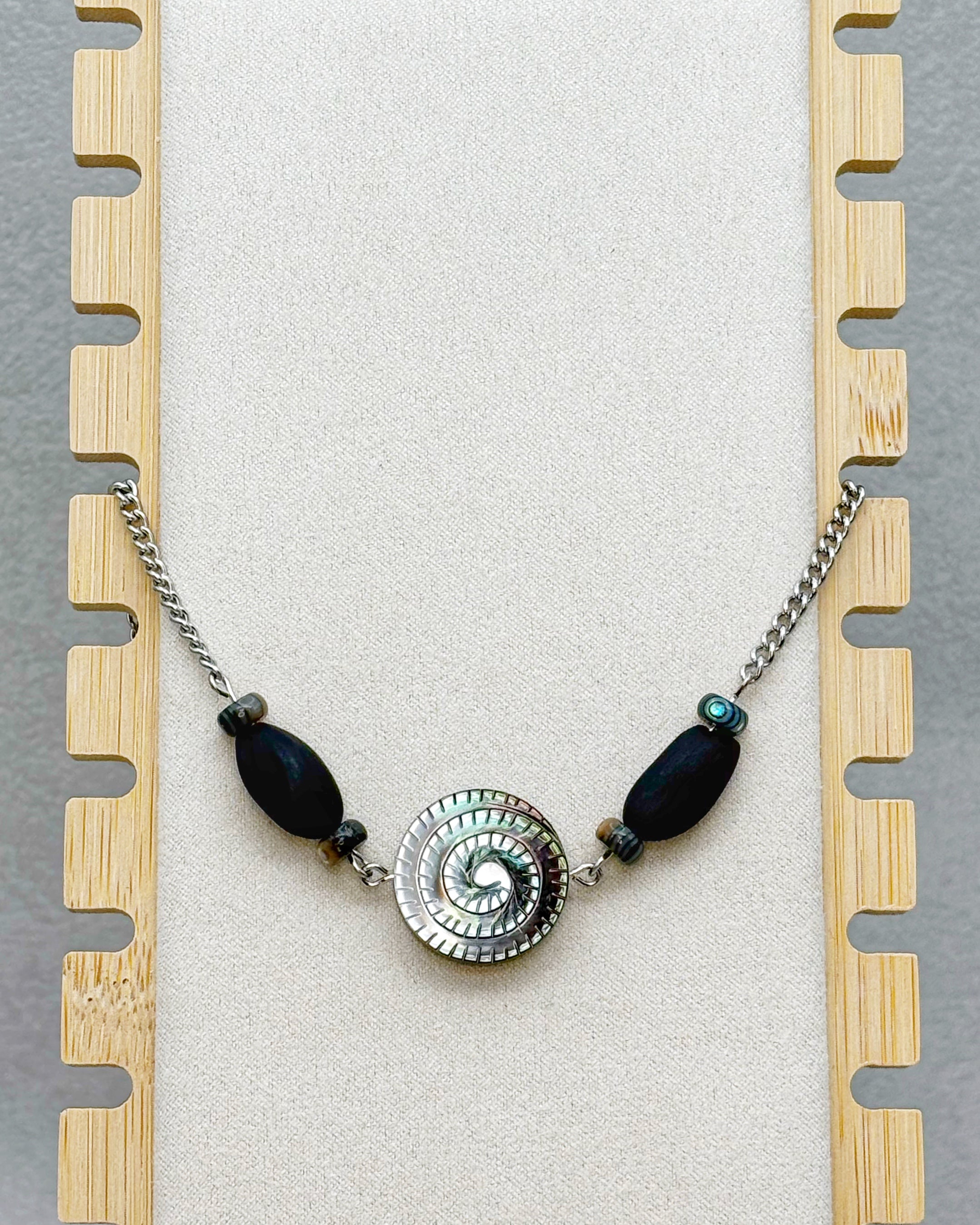 Black Lip Swirl Necklace with silver spiral centerpiece flanked by dark elongated beads on a silver chain