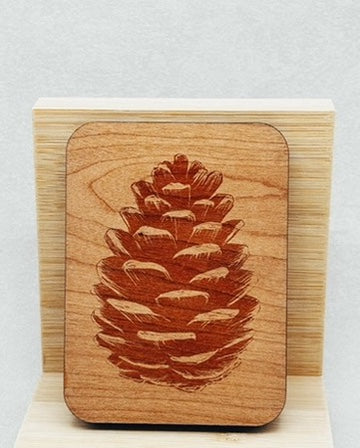 Needle Keepers with engraved pinecone design on smooth wooden surface showcasing natural grain patterns