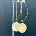 Delicate gold chain earrings featuring round iridescent discs named Mother of Pearl Simple Drops against a dark background.