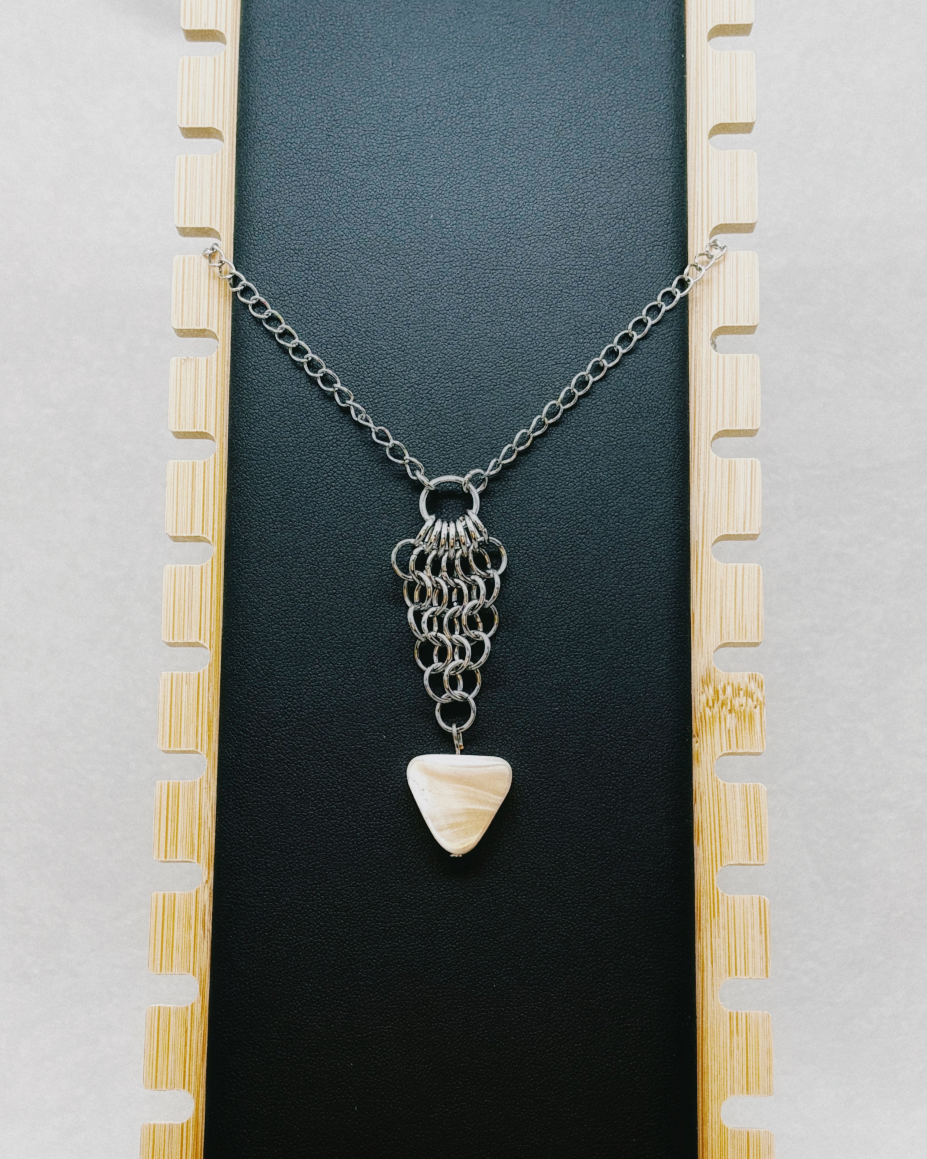 Chainmail Necklace with Shell Triangle featuring silver-tone chainmail links and a polished triangular shell pendant on black background.