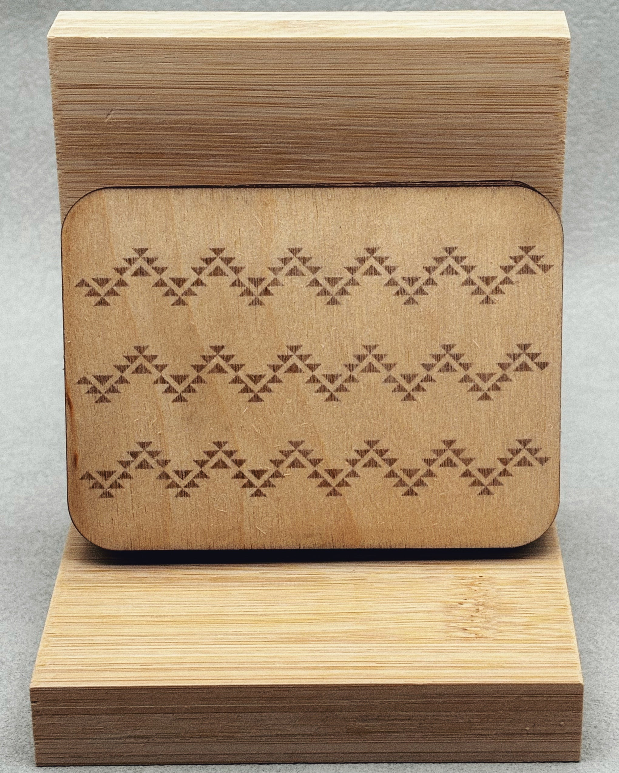 Needle Keepers wooden box with engraved symmetrical triangular pattern on smooth natural light wood surface on stand