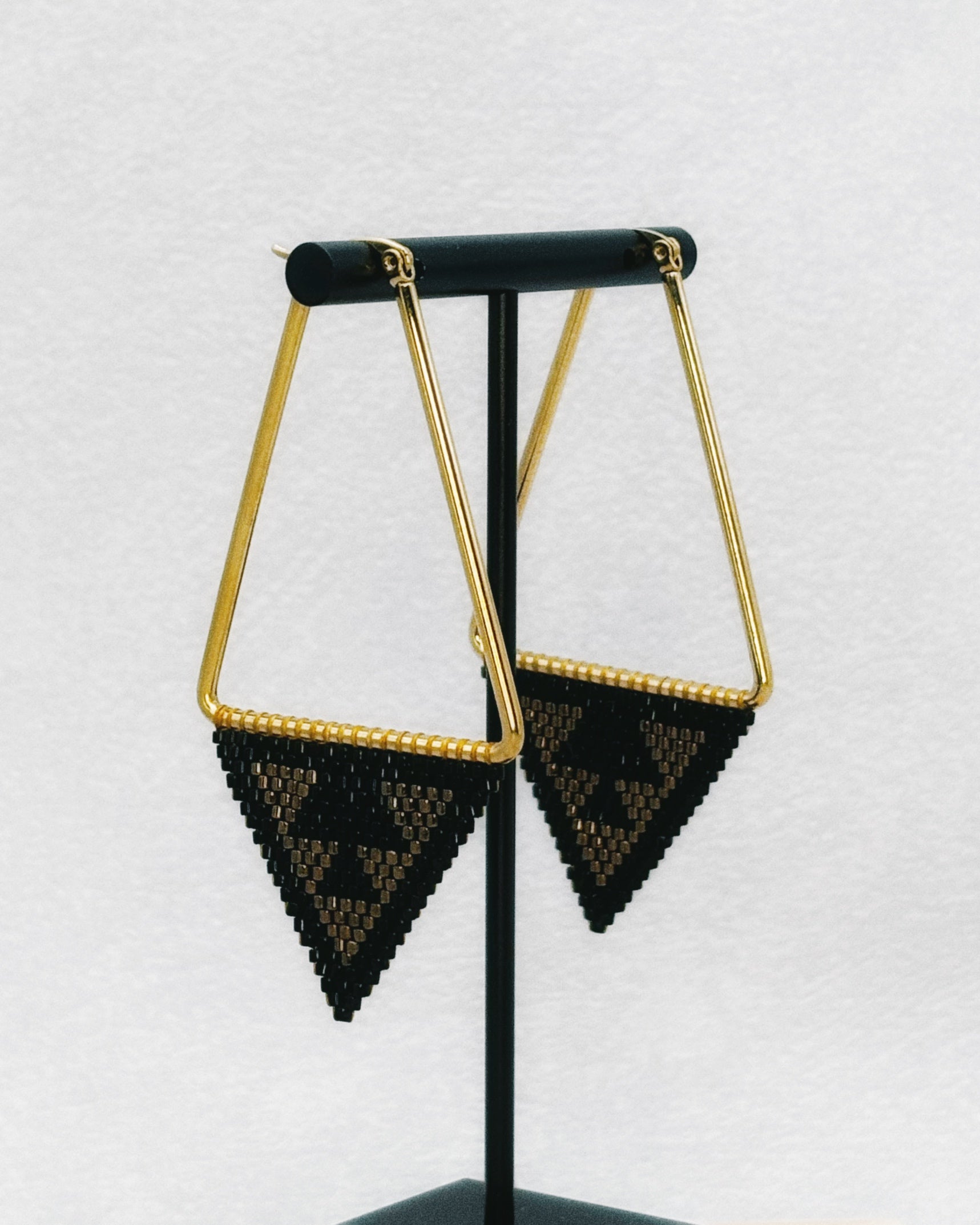 Medium Triangle Hoops featuring gold-tone triangular frames with black and gold geometric handmade beadwork accents