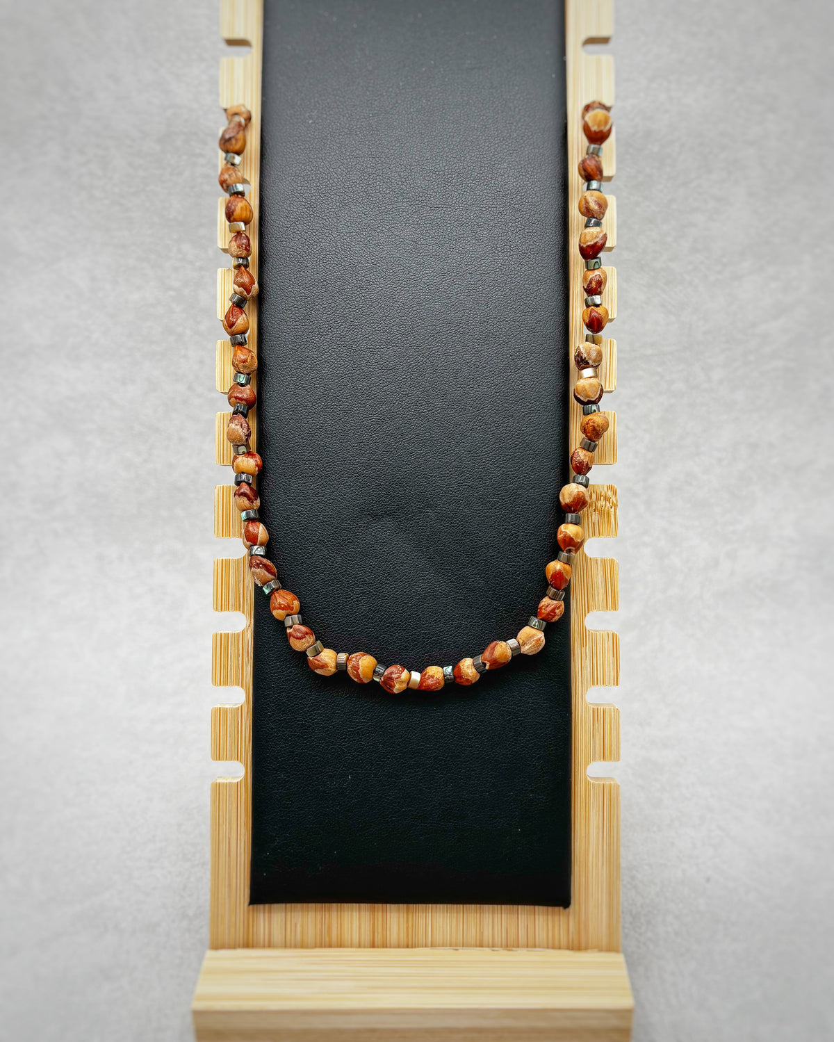 Simple Cedar Berry and Abalone Necklace with warm brown and red beads displayed on a black stand