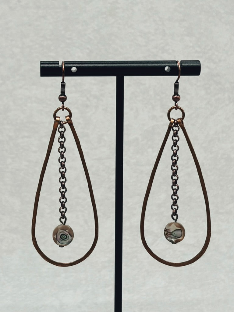 Hammered Bronze Teardrop Dangles with Faceted Abalone hanging on black stand with delicate chain and earthy tones.