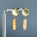Abalone Cylinder Gold Circle Studs with glossy gold discs and carved abalone cylinders suspended below against gray background