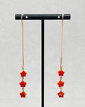 Spiny Oyster Star Drops featuring long gold chain earrings with three red star shaped stones each