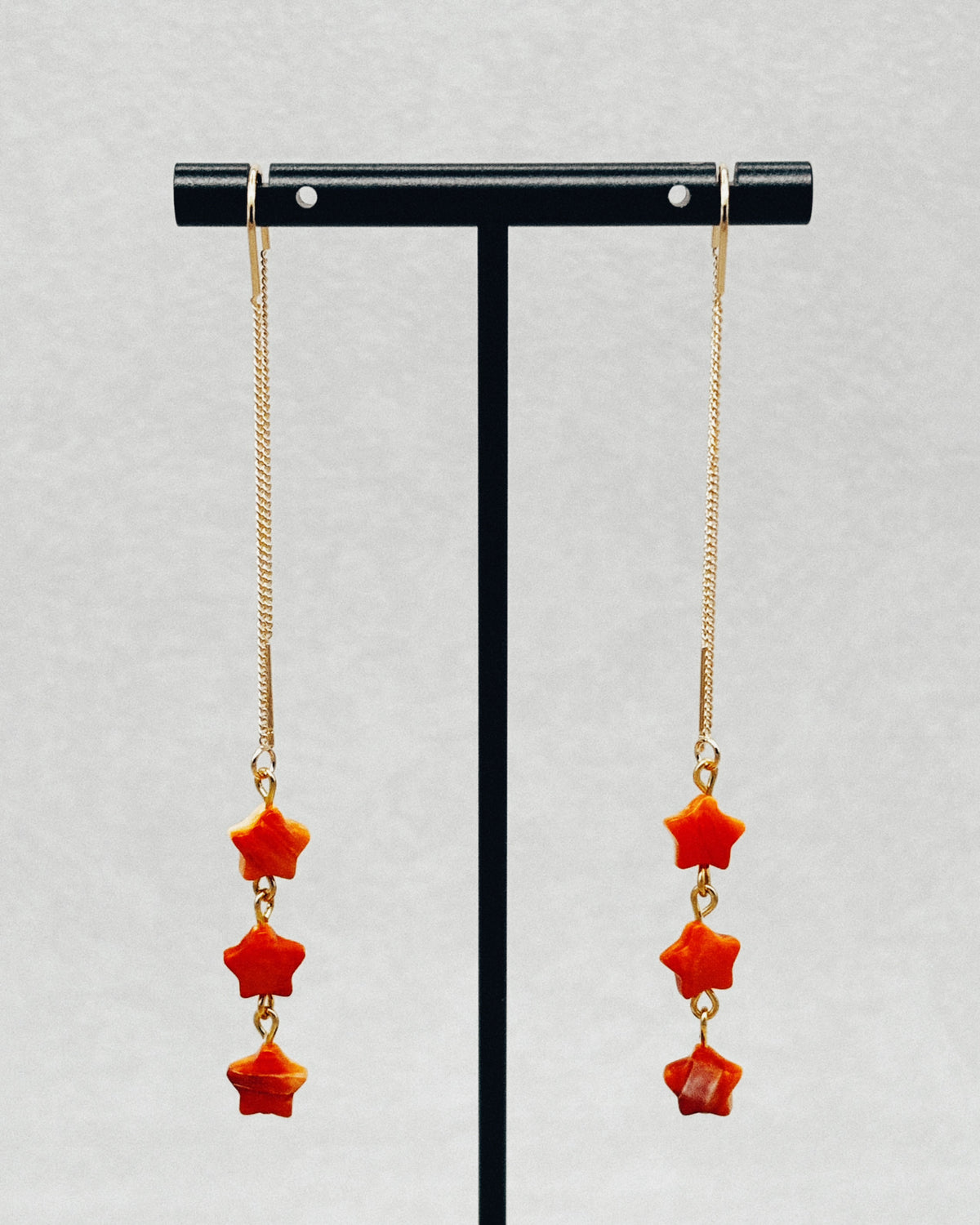 Spiny Oyster Star Drops featuring long gold chain earrings with three red star shaped stones each