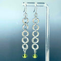 Olivine and Steel Swirl Dangles featuring linked silver rings with green olivine beads hanging on clear acrylic stand