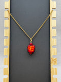 Salmonberry Necklace with vibrant red-orange beaded pendant on a gold-tone chain against black backdrop
