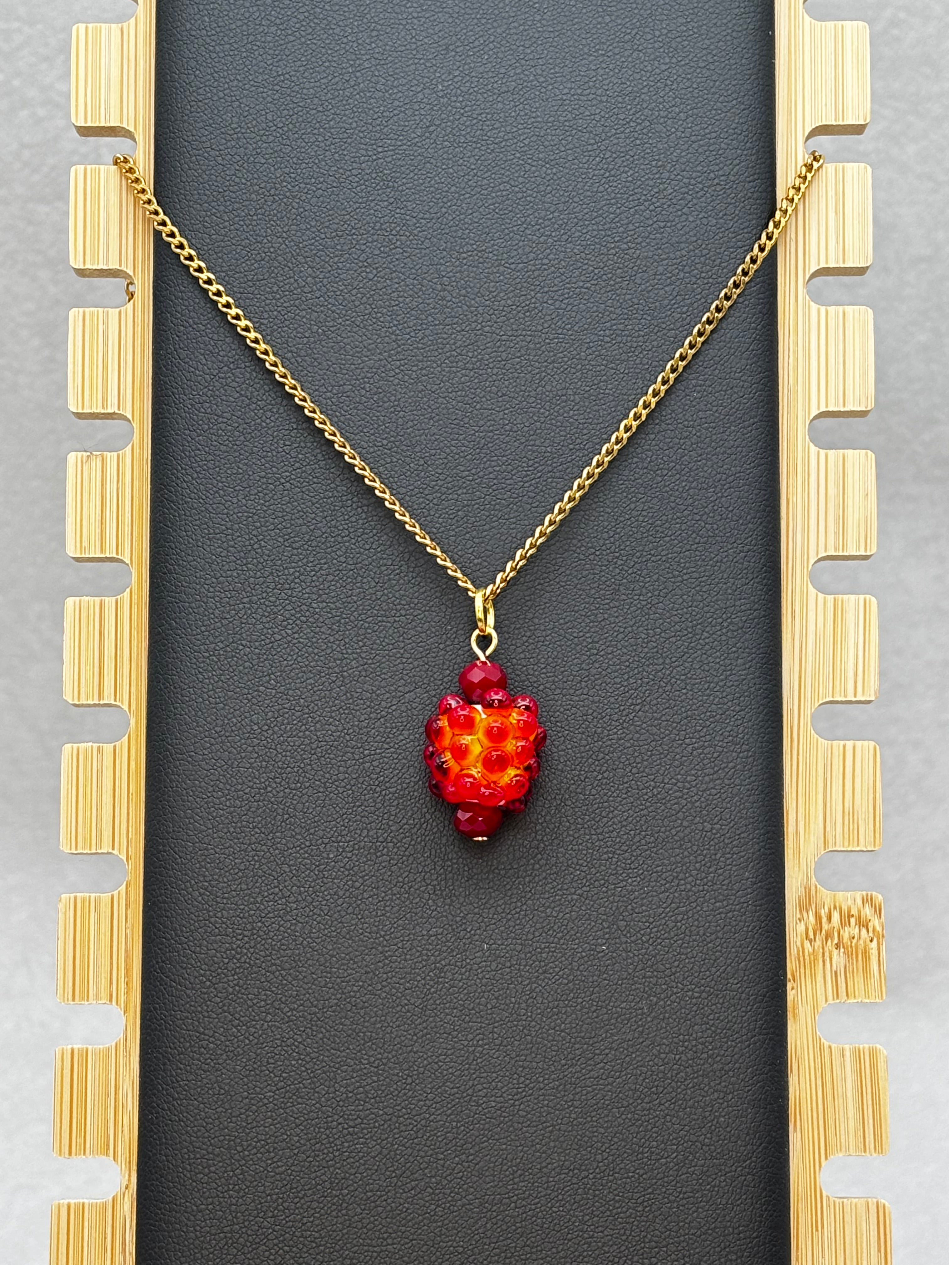 Salmonberry Necklace with vibrant red-orange beaded pendant on a gold-tone chain against black backdrop