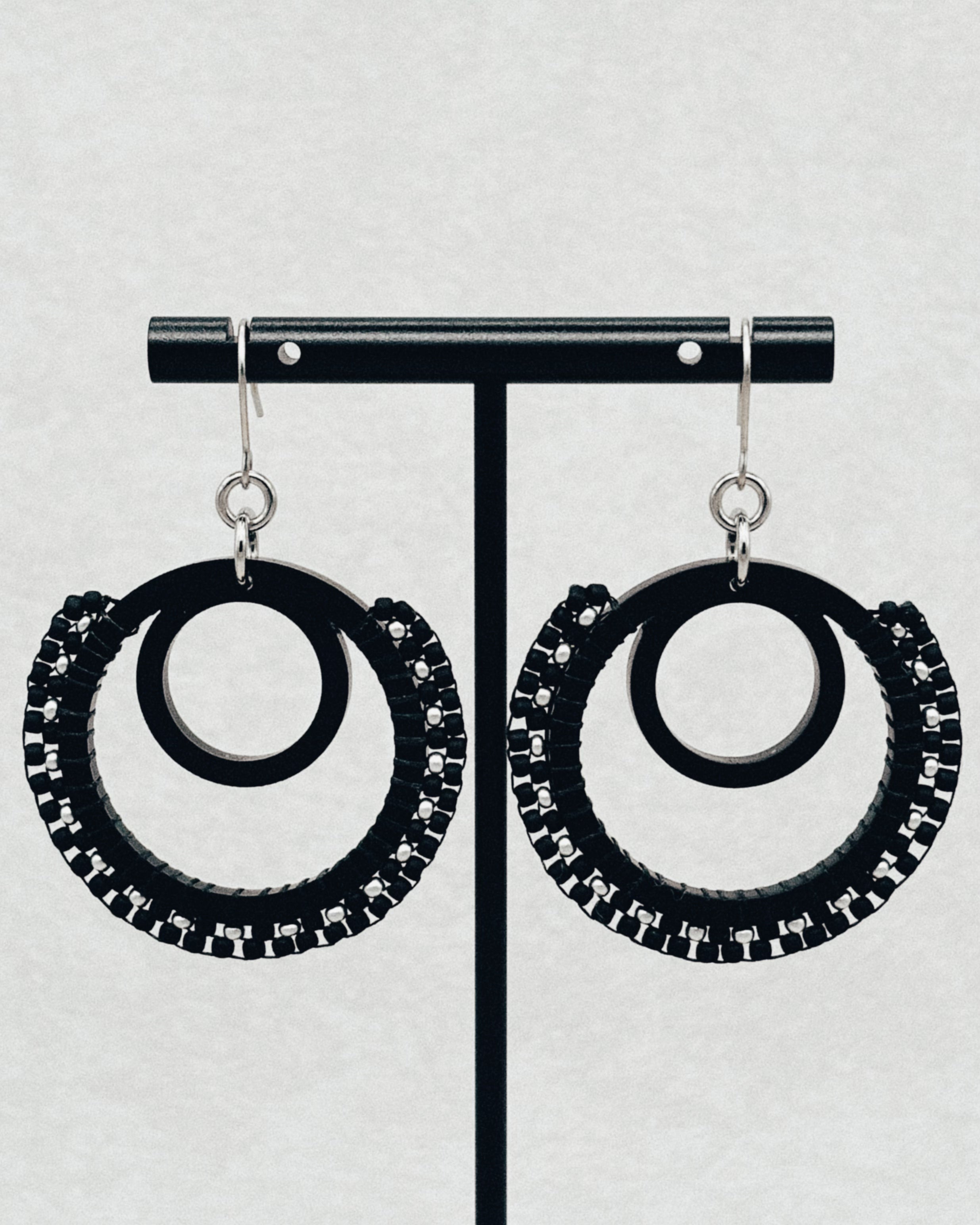 Black Brick Stitch Hoop Dangles featuring double black hoops with intricate beadwork and silver hook accents on a neutral backdrop