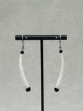 Black Dentalium Dangles hanging on a black display stand against a neutral gray background