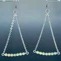 Teal Stone Silver Chain Drops with delicate silver links and matte teal and grey beads on earring hooks against blue background
