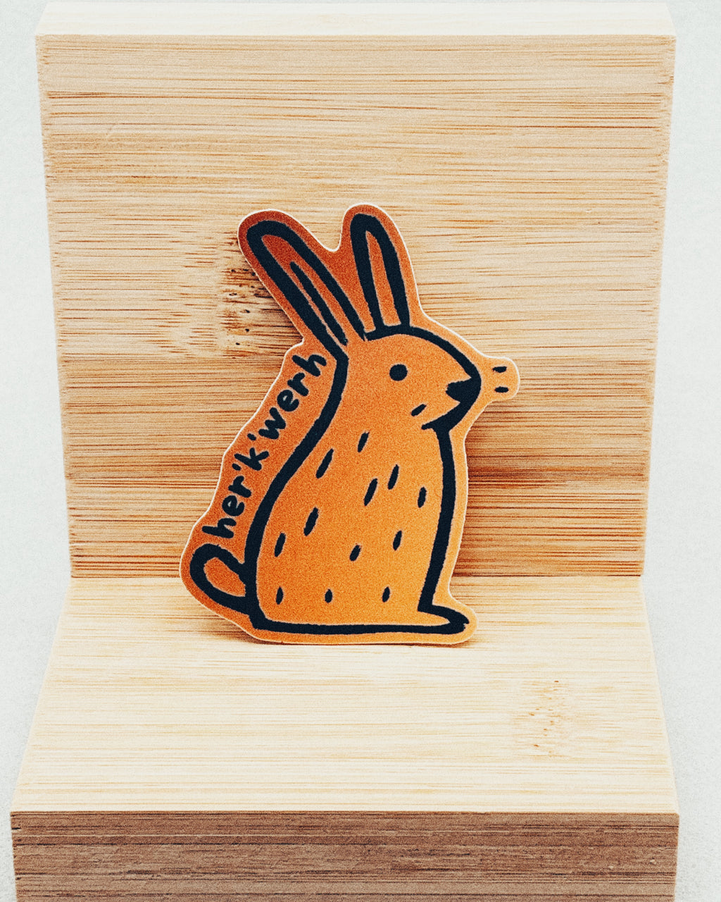 Yurok Vocabulary Stickers showing an orange rabbit illustration with black line details and Yurok word "herikwerh" on wooden background
