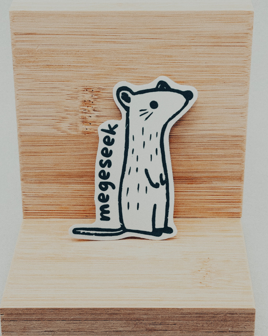 Yurok Vocabulary Stickers featuring a minimalistic black and white hand-drawn animal with the word "megesek" on wood