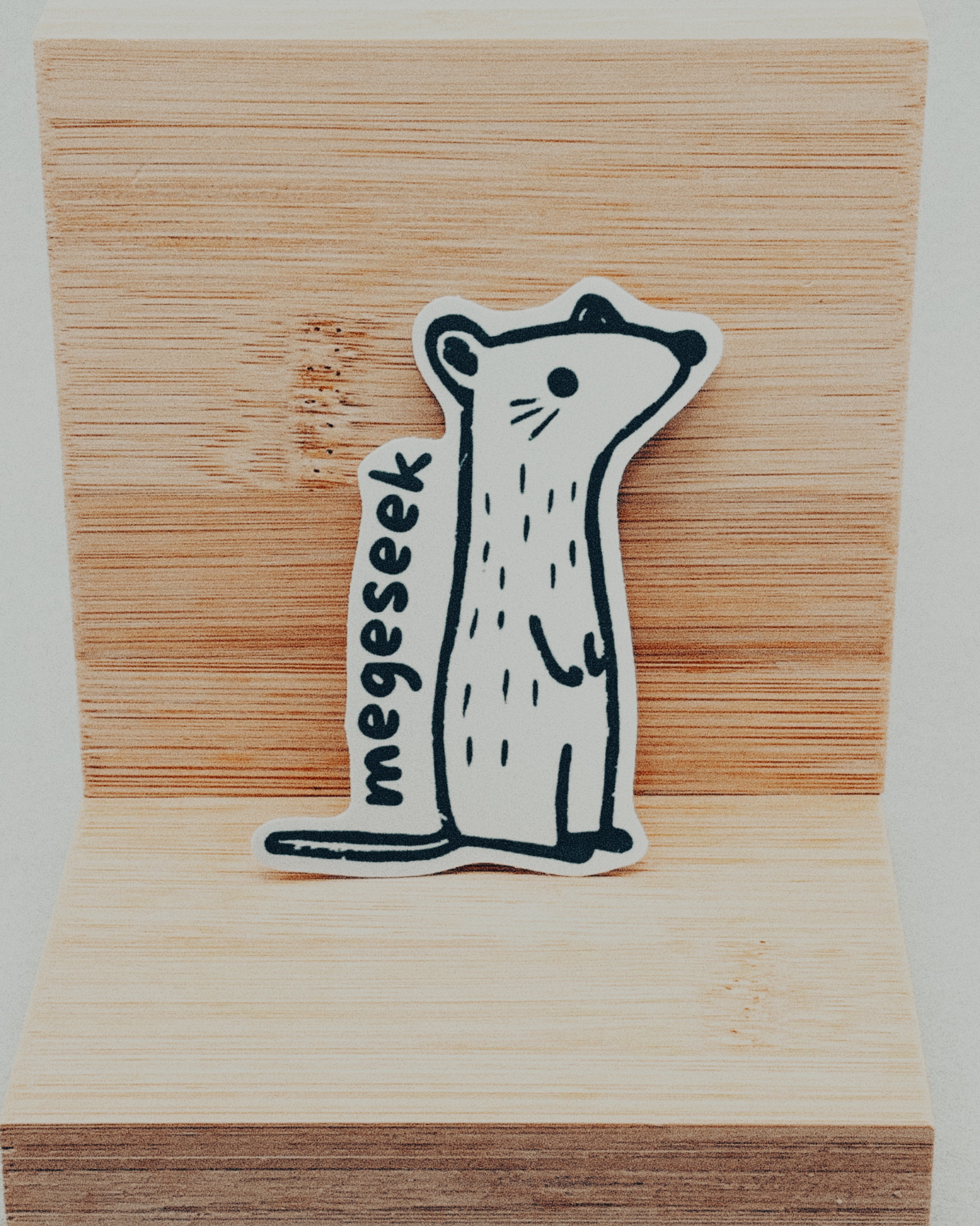 Yurok Vocabulary Stickers featuring a minimalistic black and white hand-drawn animal with the word "megesek" on wood