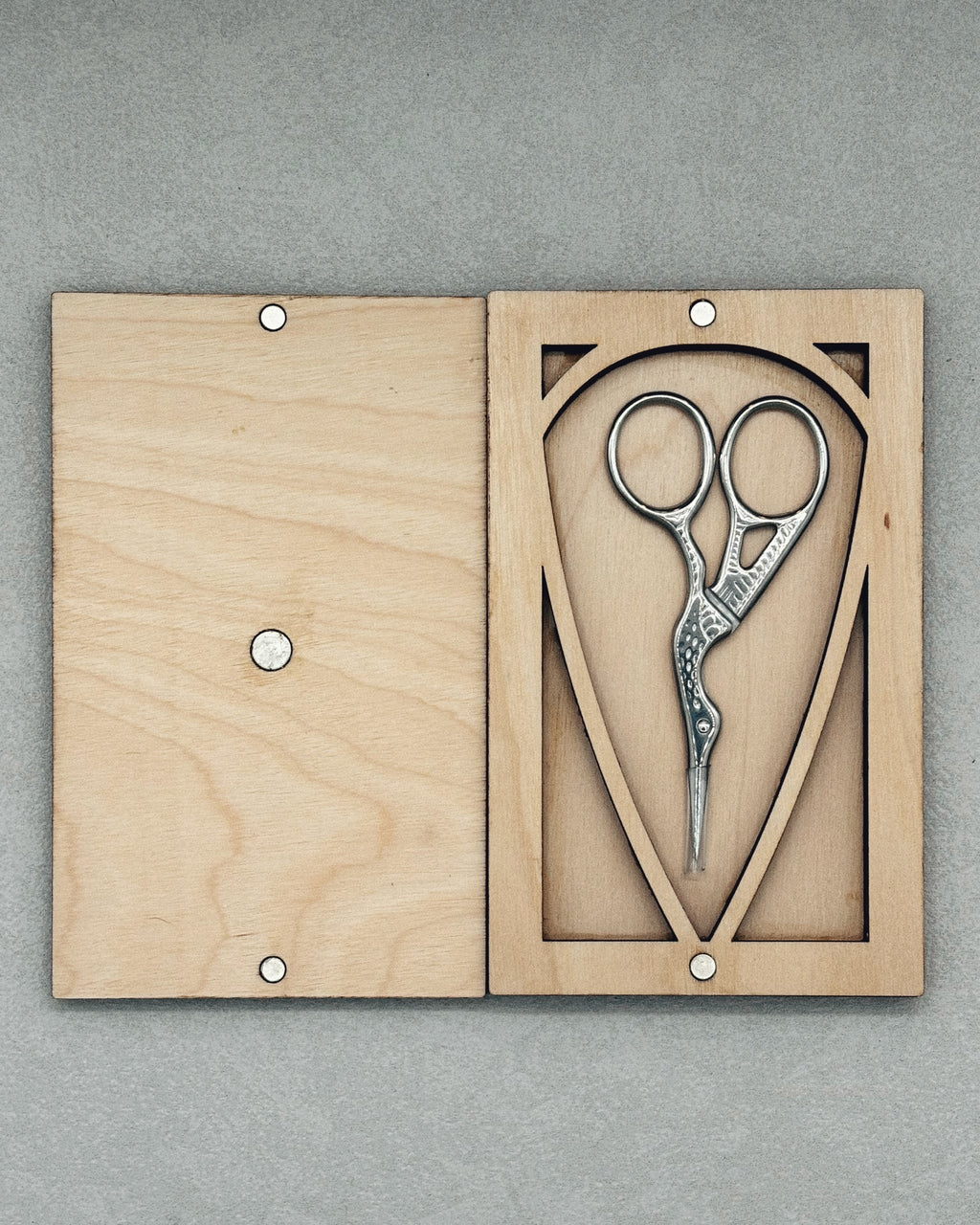 Scissor Keepers wooden case holding decorative metal scissors with a bird-shaped handle design on gray background