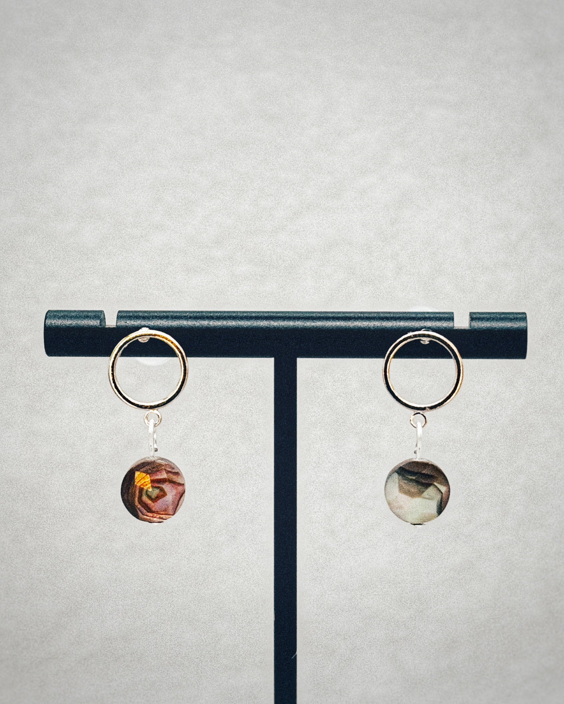 Faceted Abalone Silver Open Circle Studs featuring iridescent abalone drops on silver open circles on a display stand