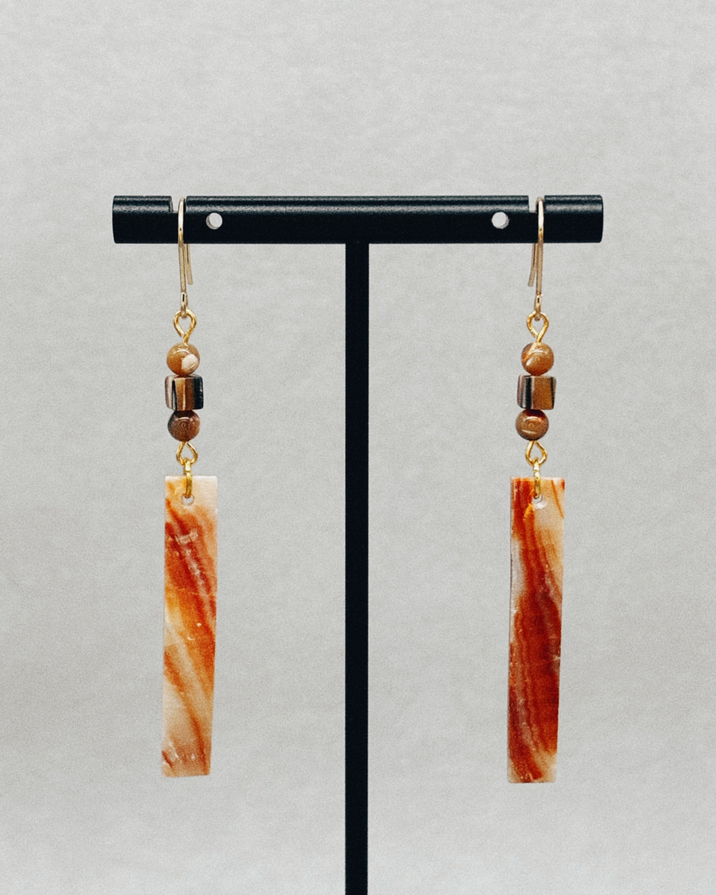 Abalone Rectangle Dangles featuring rectangular abalone pieces with brown bead accents on gold hooks hanging on a black display stand