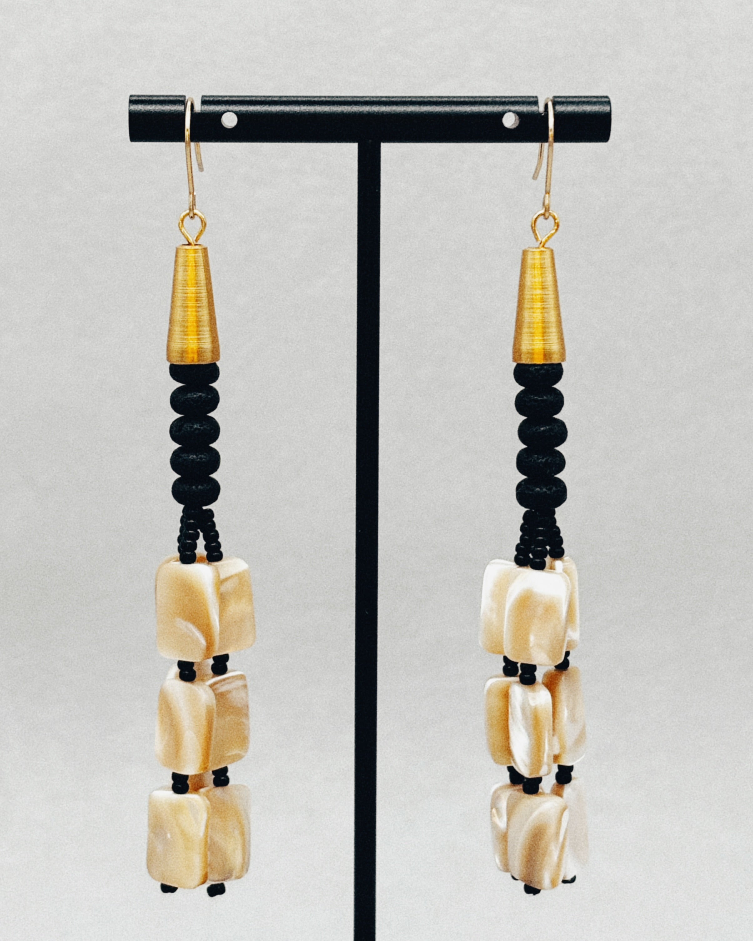 Mother of Pearl and Matte Glass Bead Dangles featuring gold accents and handcrafted black and pearl beads on display stand.
