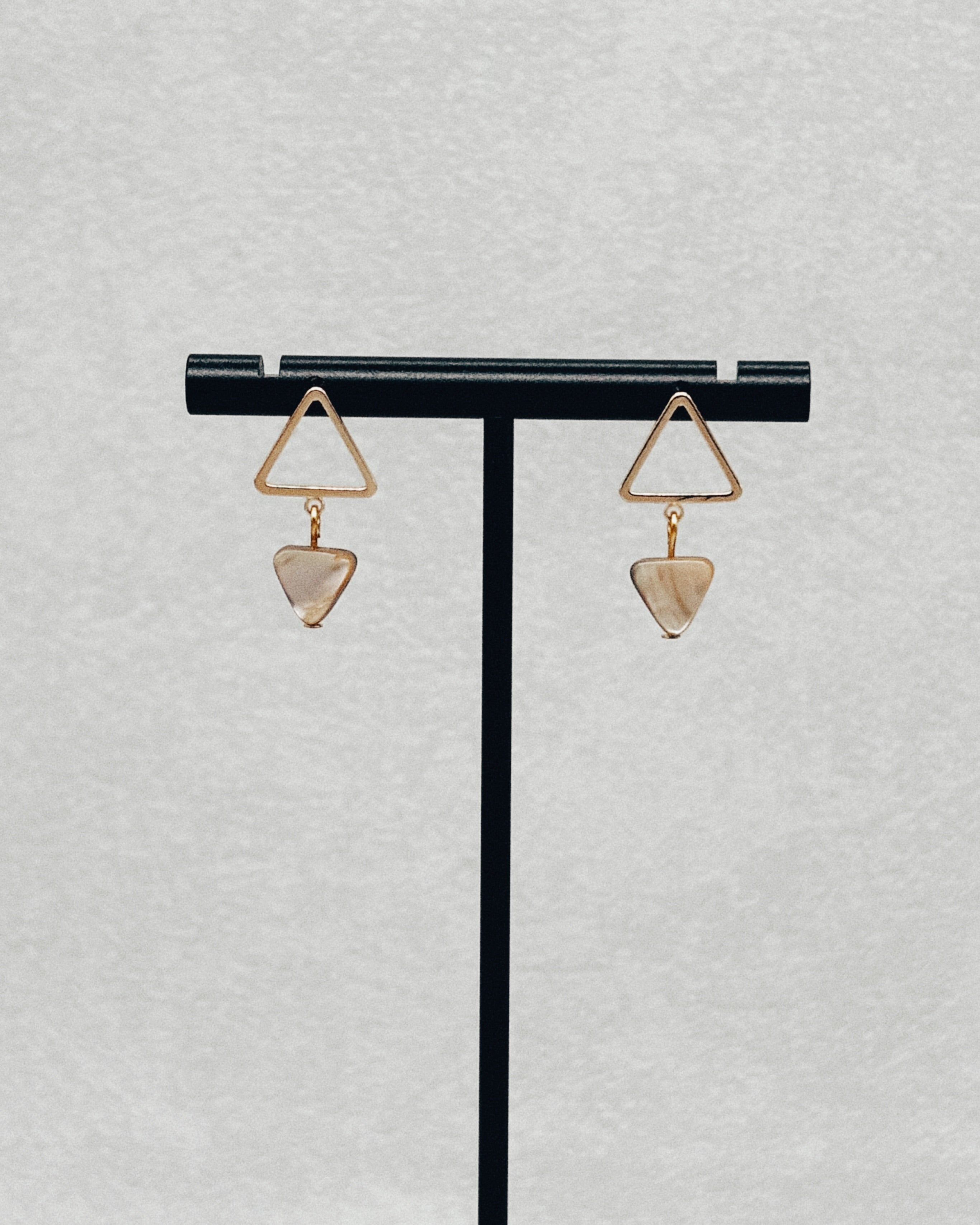 Abalone Gold Triangle Studs displayed on a black jewelry stand