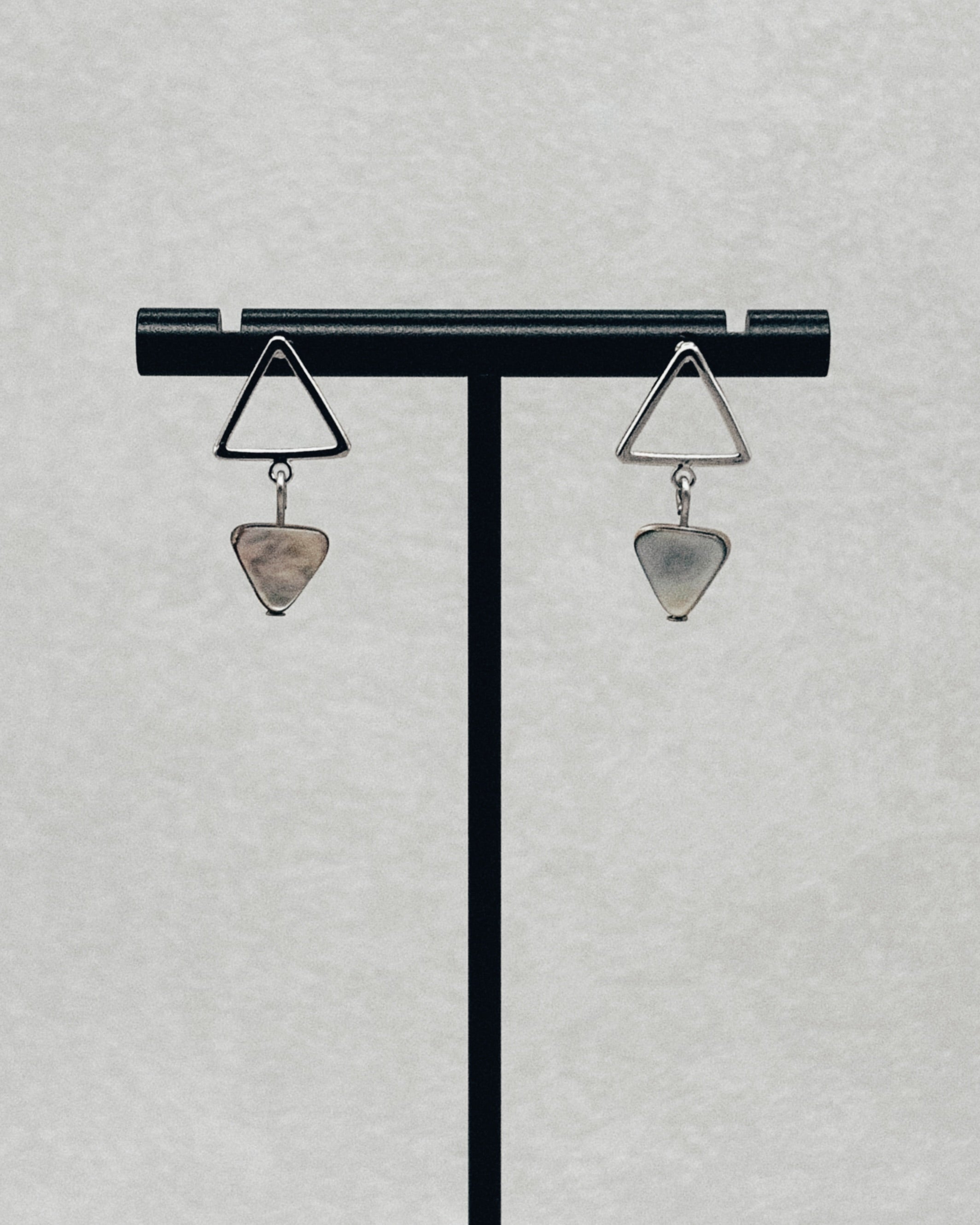 Abalone Silver Triangle Studs displayed on a black jewelry stand